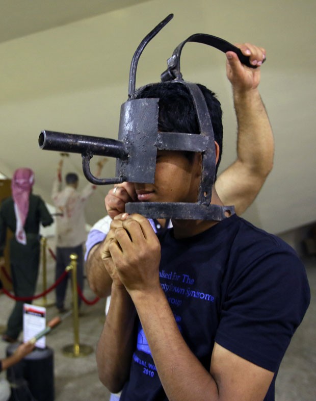 Jovem experimenta uma mãscara de tortura exposta no monumento Shaheed, em Bagdá (Foto: Ali al-Saadi/AFP)