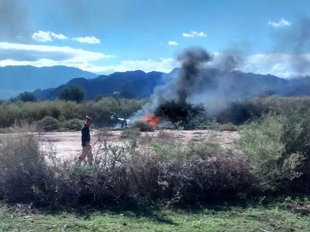 Homem passa em frente às chamas do que restou de um helicóptero envolvido no acidente aéreo envolvendo outro helicóptero durante gravação do reality show europeu 'Dropped' perto de Villa Castelli, na Argentina.