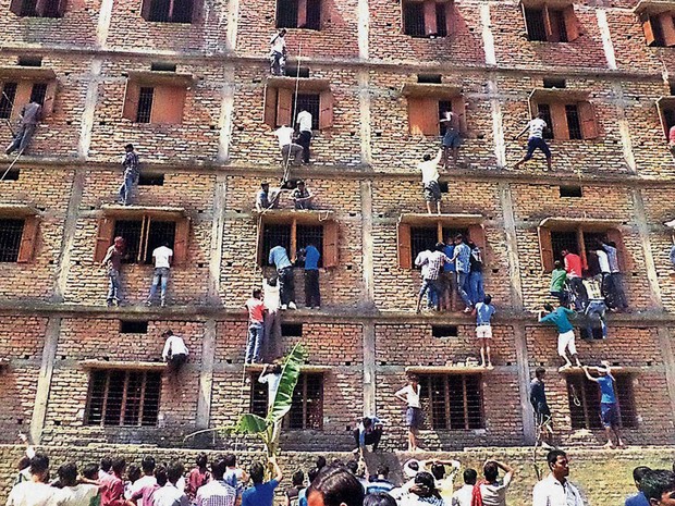Pais e parentes de estudantes indianos escalam as janelas de uma escola para passar cola aos alunos na quarta-feira (18) na cidade de Hajipur, no leste da Índia