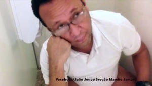 Sentado num vaso sanitário, João Jones mostra o novo clipe da banda.